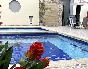Outdoor swimming pool with tropical plants and patio seating at Hotel Puerta de Oro.