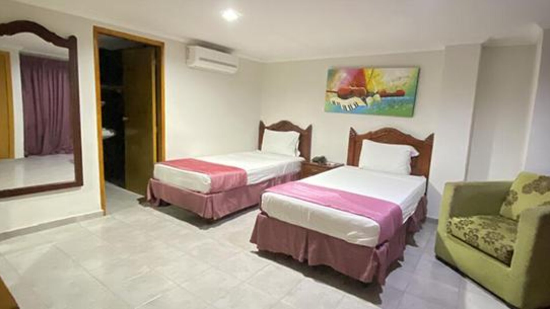 Spacious guest room with two single beds, armchair, wall mirror and colourful artwork at Hotel Puerta de Oro.