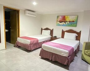 Spacious guest room with two single beds, armchair, wall mirror and colourful artwork at Hotel Puerta de Oro.