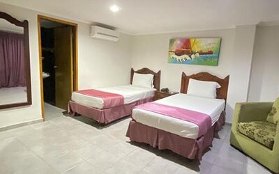 Spacious guest room with two single beds, armchair, wall mirror and colourful artwork at Hotel Puerta de Oro.