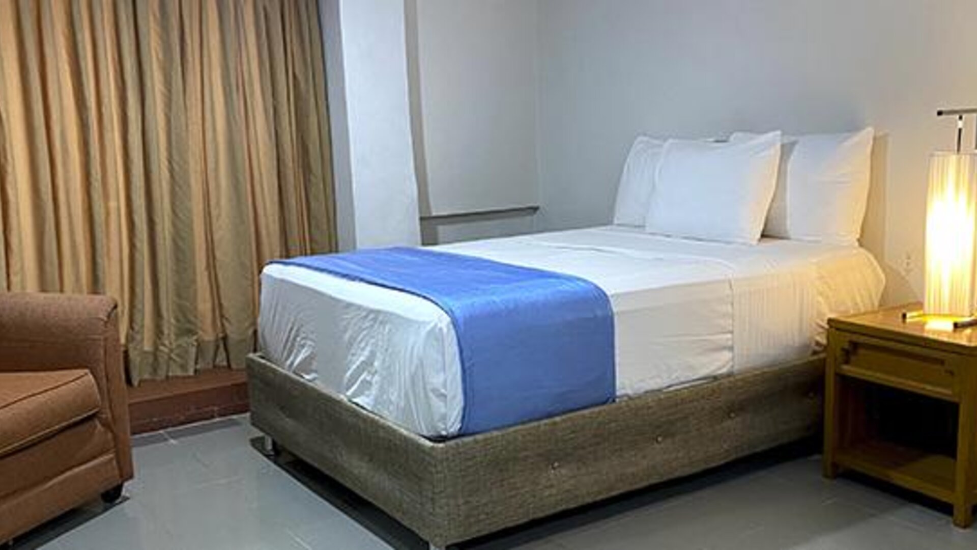 Guest room with double bed, armchair, bedside table and curtains at Hotel Puerta de Oro.