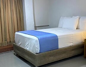 Guest room with double bed, armchair, bedside table and curtains at Hotel Puerta de Oro.