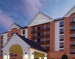 Exterior view of the multi-story Sonesta Select hotel at dusk, featuring a peach and cream façade, illuminated hotel signage, balconies, and a covered entrance.
