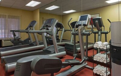 Hotel fitness center featuring treadmills, elliptical machines, cardio equipment, a mirrored wall, fresh towels, and large windows providing natural light.