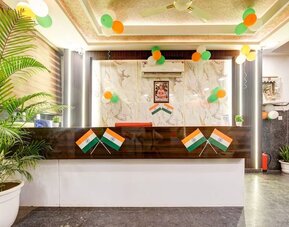 Hotel reception area decorated with Indian tricolor balloons and flags, featuring a dark wood and white front desk, marble-patterned feature wall, indoor plants and staircase to the side.