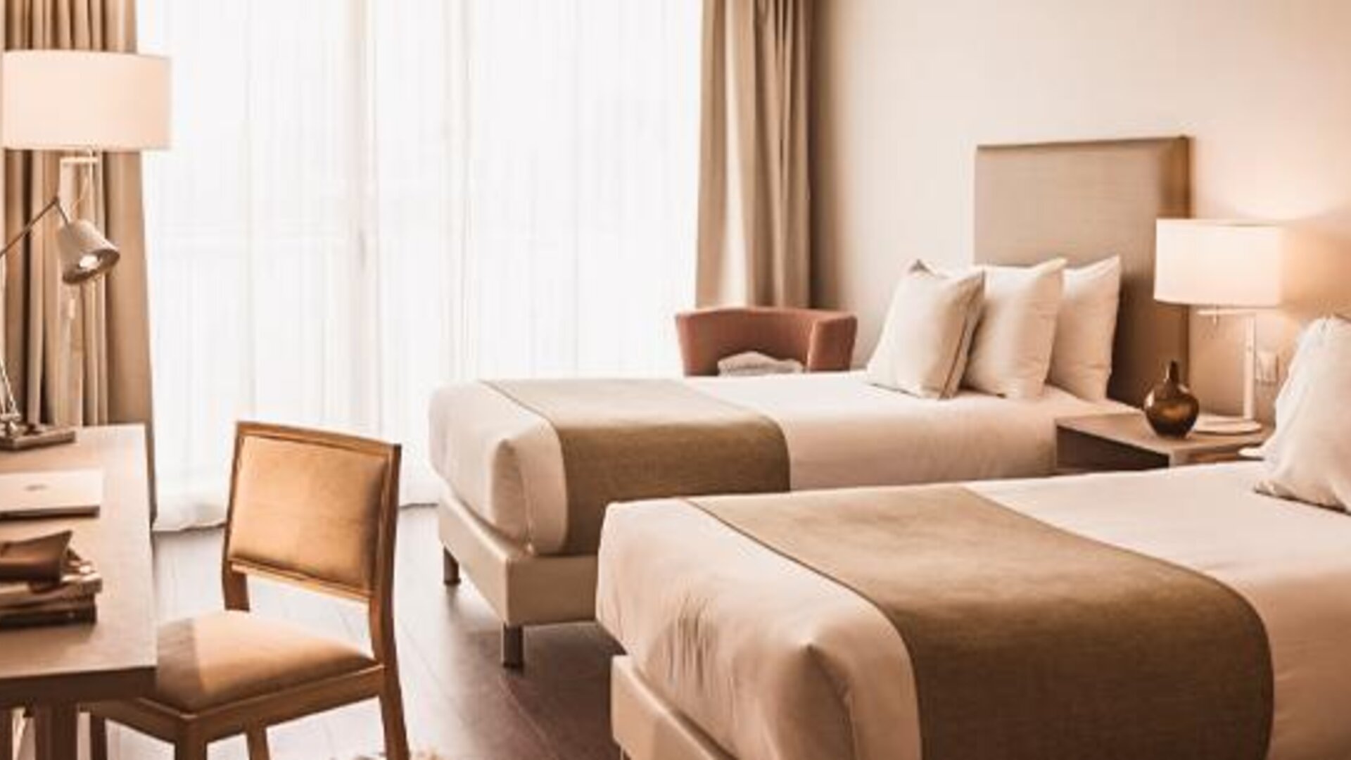 Guest room with two beds, a desk, armchair, bedside tables, and large windows with curtains at Dazzler by Wyndham Polo.