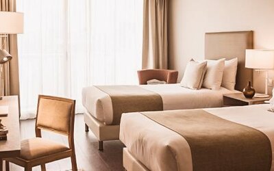 Guest room with two beds, a desk, armchair, bedside tables, and large windows with curtains at Dazzler by Wyndham Polo.