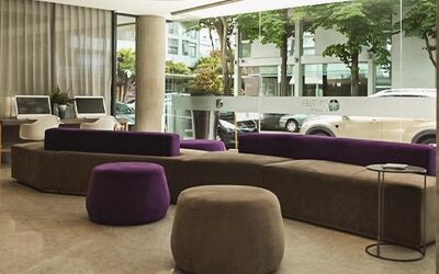 Hotel lobby with purple and gray sofas, round ottomans, floor-to-ceiling windows, and street views at Dazzler by Wyndham Polo.