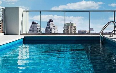 Rooftop swimming pool with a glass railing and views of surrounding city buildings at Dazzler by Wyndham Polo.
