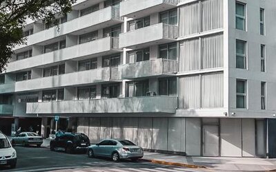 Modern multi-story hotel exterior with balconies, street-level windows, trees, and parked cars at Dazzler by Wyndham Polo.