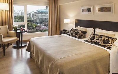 King-bed guest room with a large window overlooking city buildings, armchair, television, and bedside tables at El Conquistador Hotel.