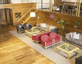 Hotel lounge with wood flooring, red and gray armchairs, sofas, coffee tables, and framed artwork at El Conquistador Hotel