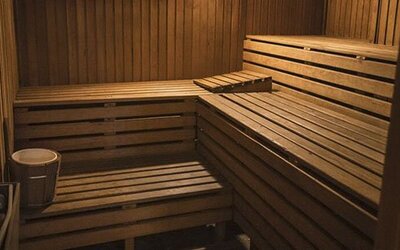Wood-paneled sauna with tiered benches, a heater, and bucket inside at El Conquistador Hotel.