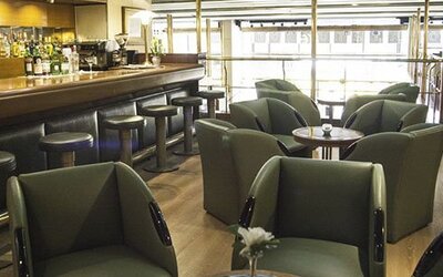 Hotel bar and lounge with green armchairs, round tables, bar stools, and large windows at El Conquistador Hotel.