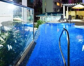 Outdoor swimming pool with blue water, glass panels, lounge chairs, and umbrellas at Hotel Grand International.