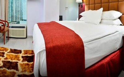Guest room with a king bed, red runner, wood furnishings, desk, and large windows overlooking city buildings at Hotel Grand International.