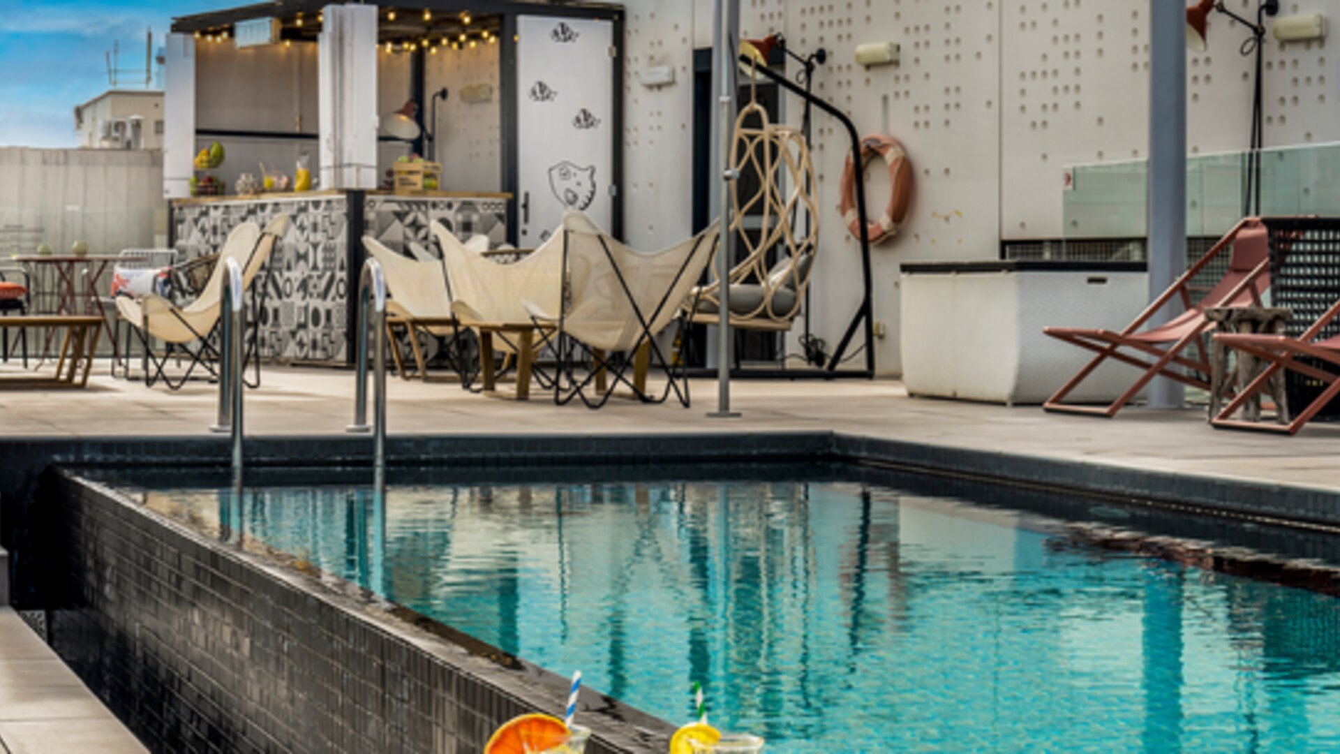 Rooftop terrace overlooking the city with a swimming pool, lounge chairs, canopy, and outdoor bar at Hotel ibis Styles Barcelona City Bogatell.