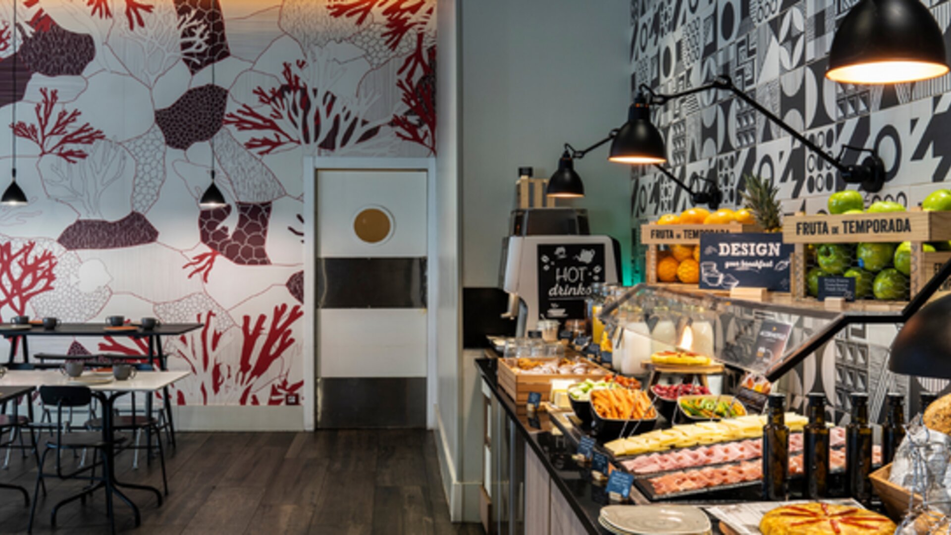 Dining area with rows of tables and chairs, pendant lights, sofas, and patterned decorative walls at Hotel ibis Styles Barcelona City Bogatell.