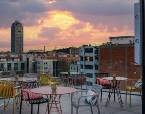 Rooftop terrace with colorful chairs, round tables, lounge seating, and city views at Hotel ibis Styles Barcelona City Bogatell.