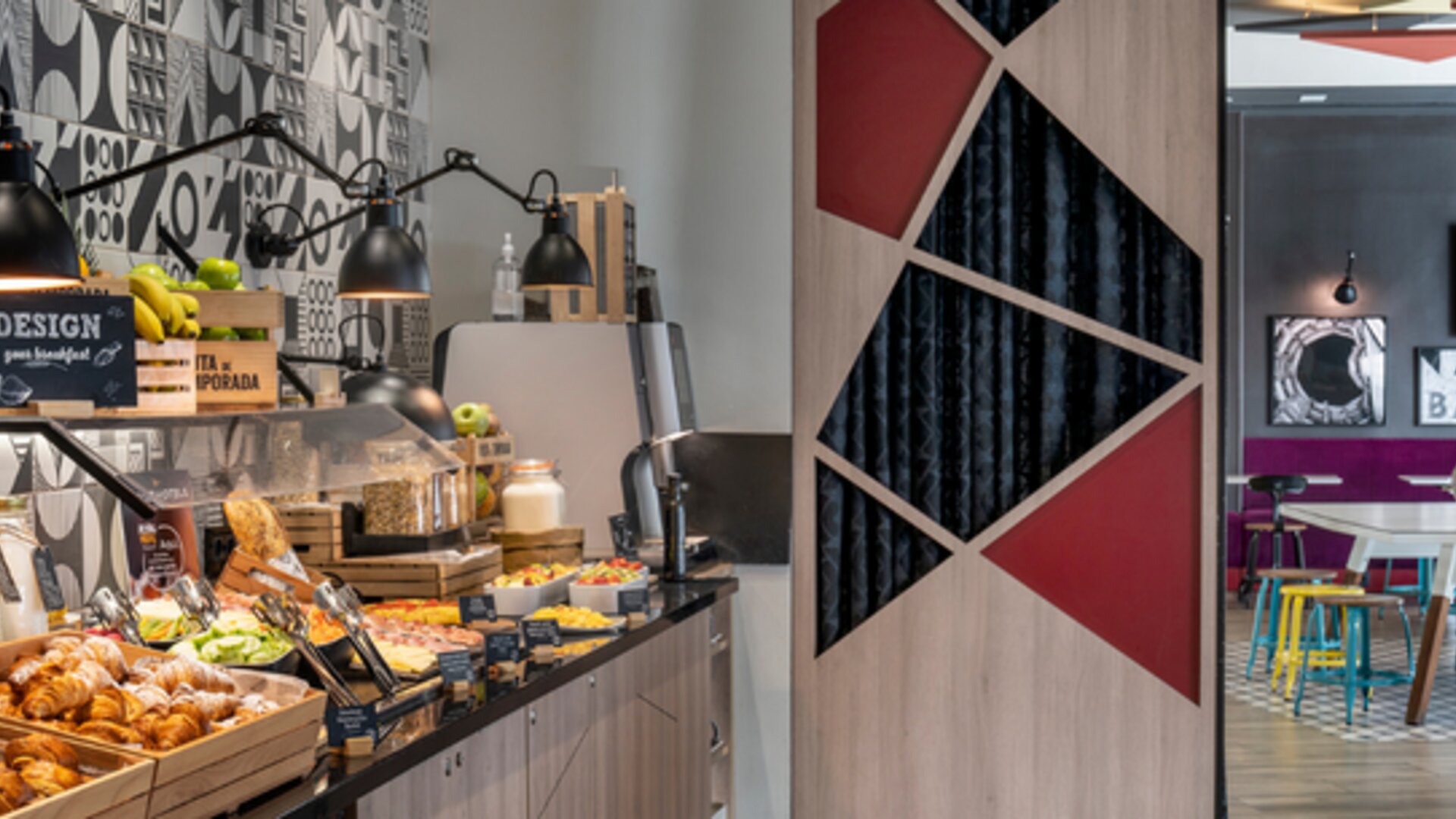 Breakfast buffet with pastries, fruit, drinks, and food displays beneath black pendant lamps at Hotel ibis Styles Barcelona City Bogatell.