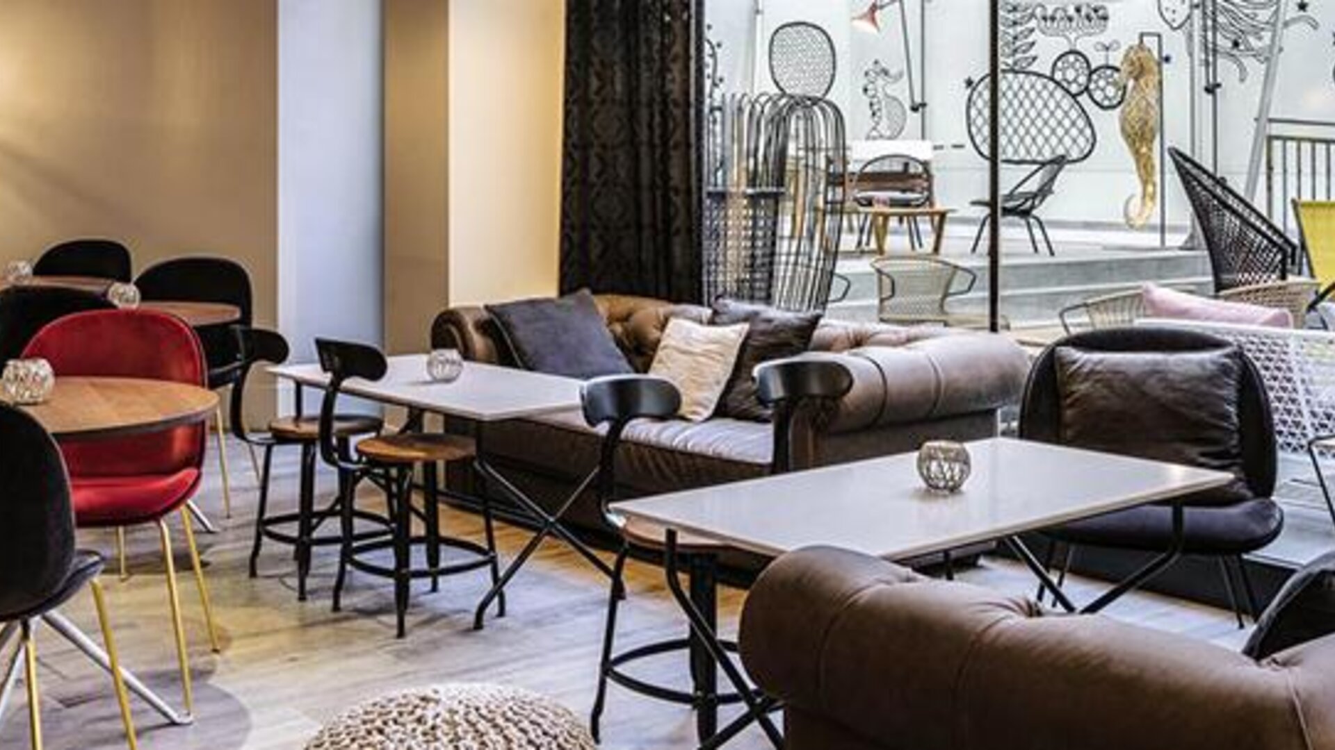 Indoor lounge with sofas, armchairs, round tables, pendant lighting, and views of the rooftop terrace at Hotel ibis Styles Barcelona City Bogatell.