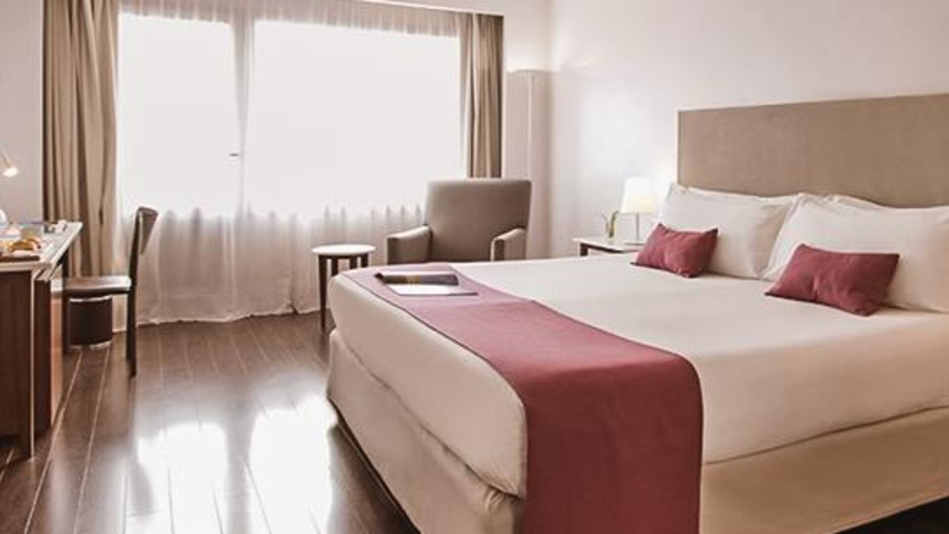 Guest room with a king bed, pink runner and pillows, armchair, desk, bedside tables, and large window at Dazzler by Wyndham Buenos Aires Recoleta.