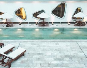 Indoor swimming pool with tiled deck, loungers, tables, umbrellas, and curved windows at Dazzler by Wyndham Buenos Aires Recoleta.