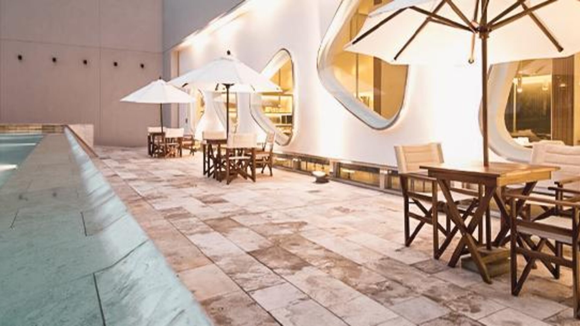 Indoor pool terrace with tables, chairs, umbrellas, curved windows, and poolside seating at Dazzler by Wyndham Buenos Aires Recoleta.