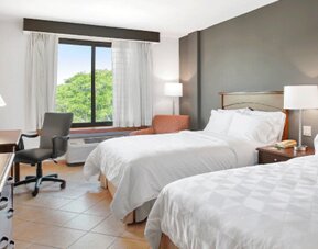 Guest room with two beds, bedside table, desk, office chair and large window overlooking greenery at Holiday Inn Panama Canal.