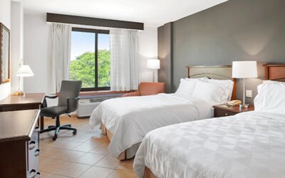 Guest room with two beds, bedside table, desk, office chair and large window overlooking greenery at Holiday Inn Panama Canal.