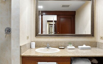 Hotel bathroom with a granite vanity, sink, large mirror and tiled shower at Holiday Inn Panama Canal.