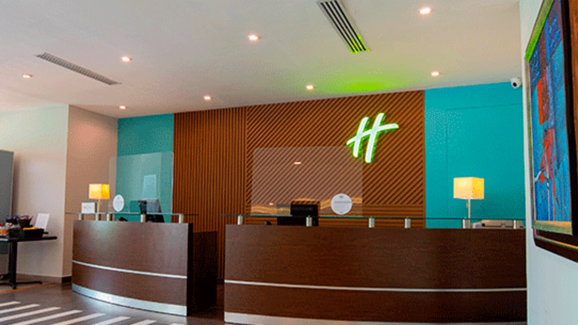 Hotel reception desk with modern wood paneling, teal walls and Holiday Inn branding at Holiday Inn Panama Canal.