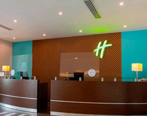 Hotel reception desk with modern wood paneling, teal walls and Holiday Inn branding at Holiday Inn Panama Canal.