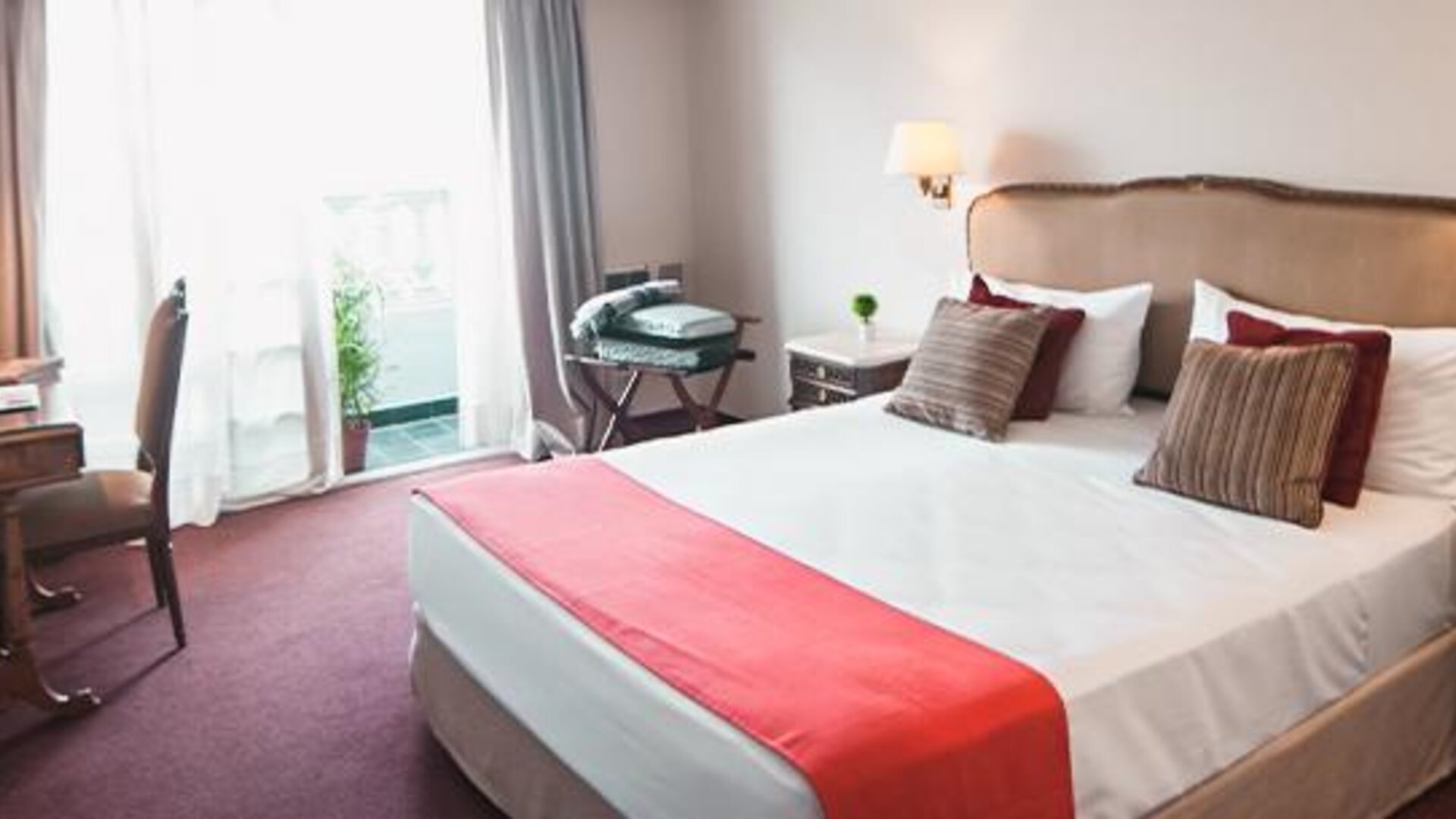 Guest room with a double bed, white linens, red bed runner, desk and balcony doors at Ramada by Wyndham Buenos Aires Centro.