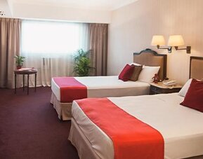 Guest room with two twin beds, white linens, red bed runners, red accent pillows and a large window at Ramada by Wyndham Buenos Aires Centro.