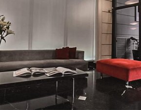 Hotel lounge with a gray sofa, red ottoman, marble coffee table and open books at Ramada by Wyndham Buenos Aires Centro.