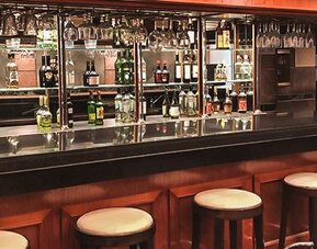 Hotel bar with a dark wood counter, stools, liquor bottles and hanging glassware at Ramada by Wyndham Buenos Aires Centro.