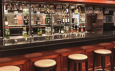 Hotel bar with a dark wood counter, stools, liquor bottles and hanging glassware at Ramada by Wyndham Buenos Aires Centro.