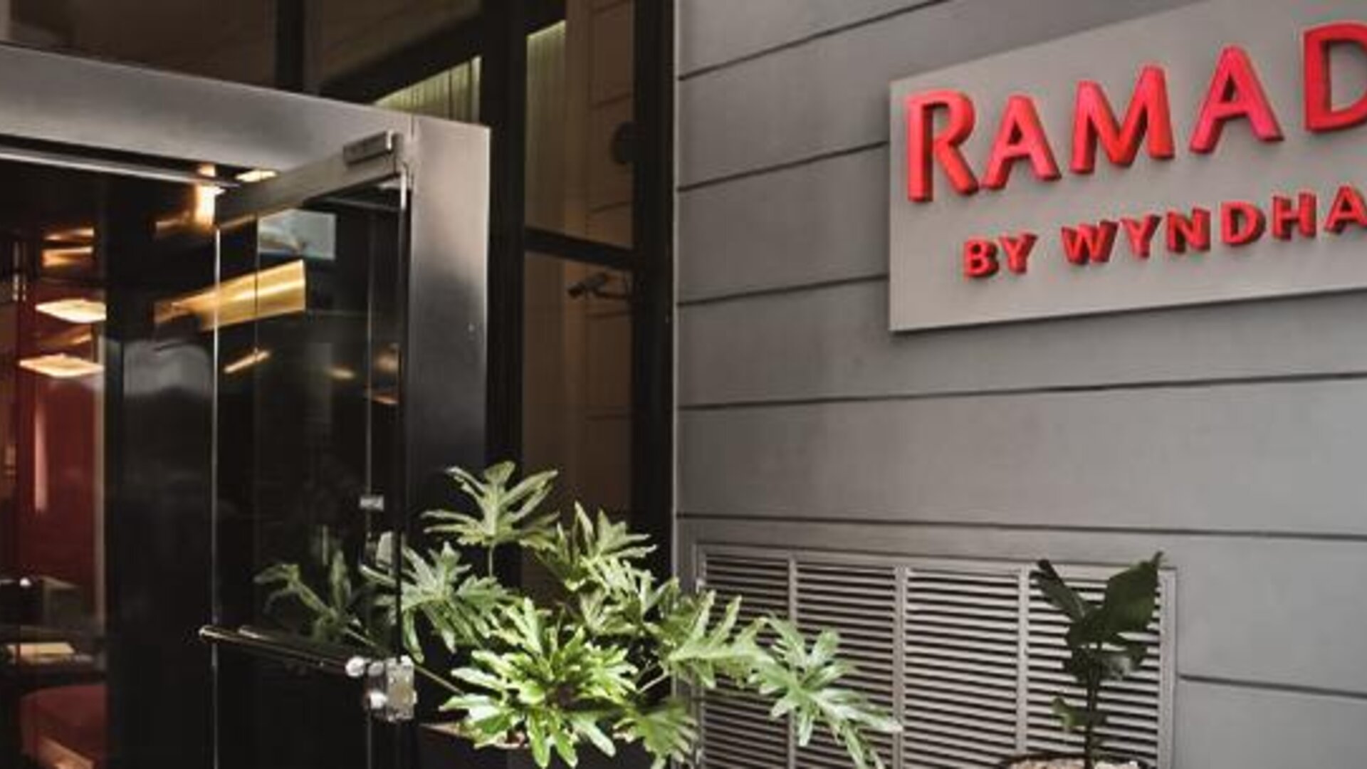 Hotel entrance with glass doors, illuminated Ramada by Wyndham signage and potted plants at Ramada by Wyndham Buenos Aires Centro.