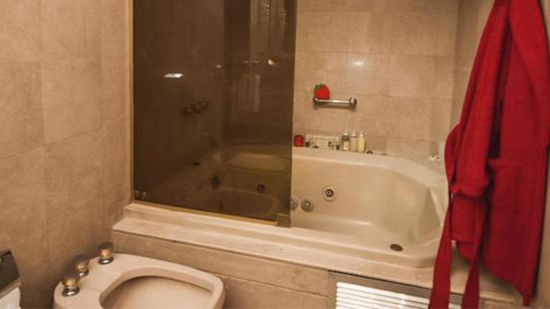 Bathroom with a whirlpool bathtub, glass shower enclosure and red bathrobe at Ramada by Wyndham Buenos Aires Centro.