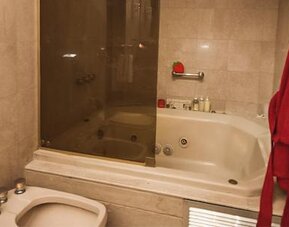 Bathroom with a whirlpool bathtub, glass shower enclosure and red bathrobe at Ramada by Wyndham Buenos Aires Centro.
