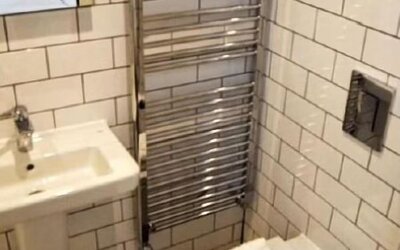 Bathroom with white subway-tile walls, a wall-mounted sink, heated towel rail, toilet and folded white towels at Victoria Inn.