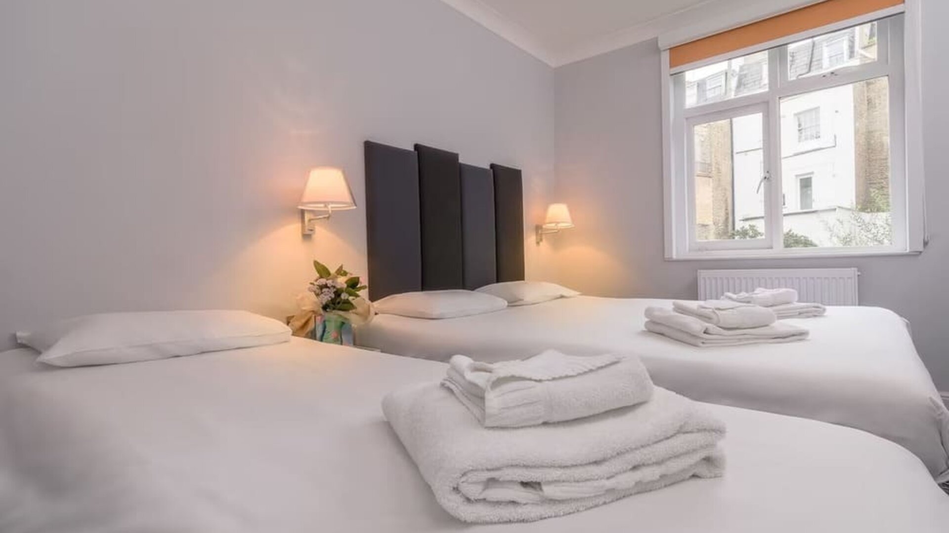 Guest room with two single beds, white linens, folded towels, bedside lamps and a large window at Victoria Inn.