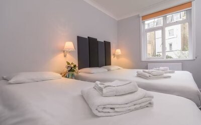 Guest room with two single beds, white linens, folded towels, bedside lamps and a large window at Victoria Inn.