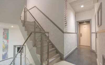 Interior staircase and hallway at Victoria Inn with glass stair railings, gray flooring, white walls and guest room doors.