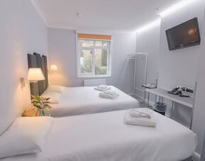 Double guest room with a white bed, dark upholstered headboard, bedside tables, wall-mounted reading lights and a large window at Victoria Inn.