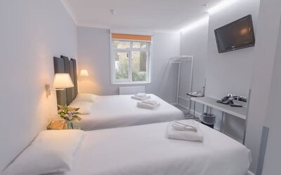 Double guest room with a white bed, dark upholstered headboard, bedside tables, wall-mounted reading lights and a large window at Victoria Inn.