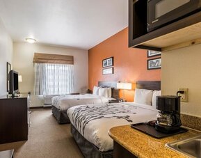 Double guest room with two beds, white bedding, orange accent wall, bedside lamps, television, microwave, refrigerator, coffee maker, and kitchenette counter at Sleep Inn & Suites Stafford - Sugar Land.