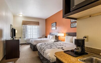 Double guest room with two beds, white bedding, orange accent wall, bedside lamps, television, microwave, refrigerator, coffee maker, and kitchenette counter at Sleep Inn & Suites Stafford - Sugar Land.