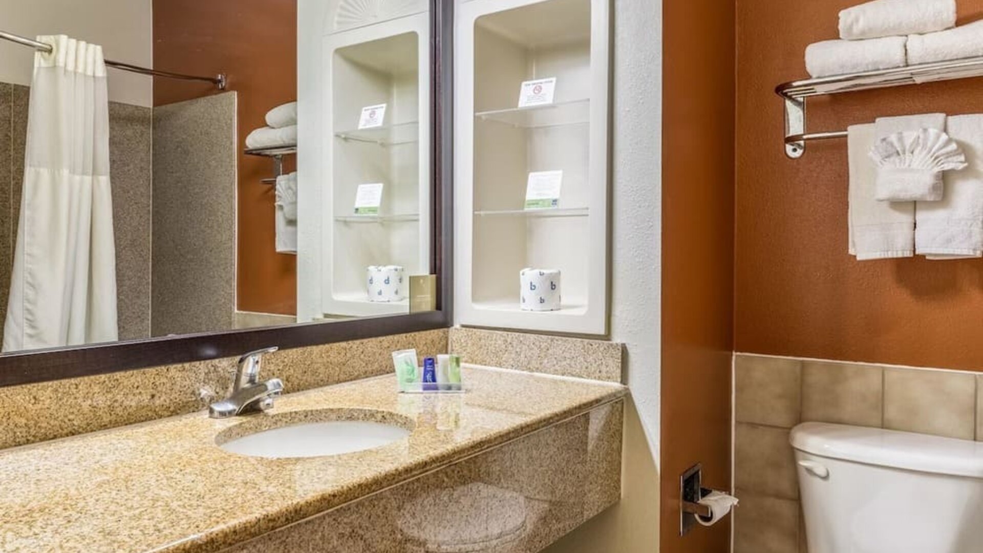 Bathroom with a granite vanity, white sink, large mirror, toiletries, towel rack with folded towels, and toilet at Sleep Inn & Suites Stafford - Sugar Land.